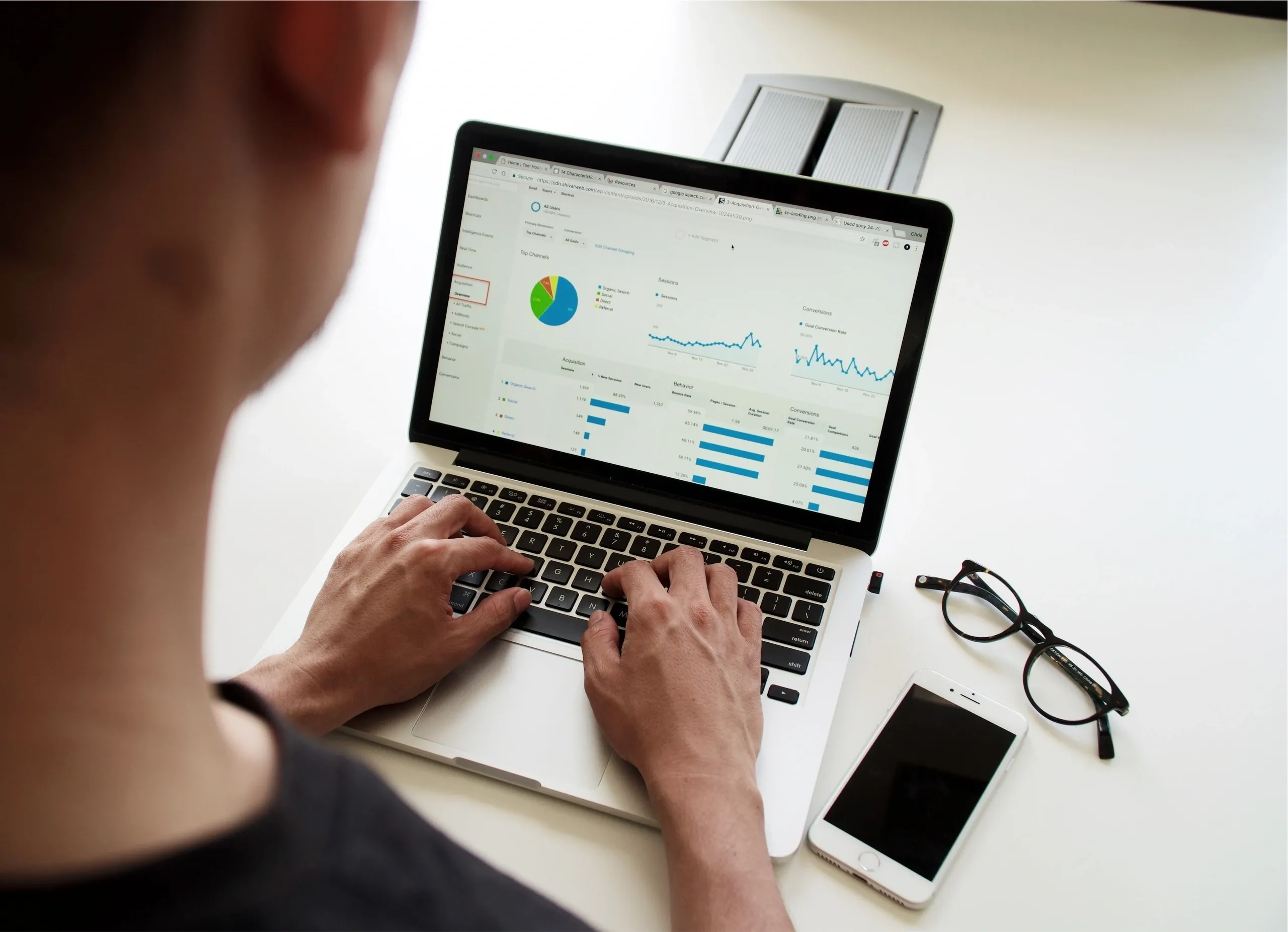 Person working on a laptop with analytics charts and a smartphone beside it